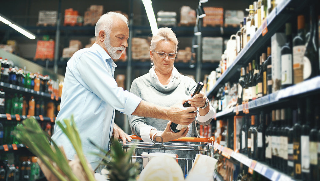 Older couple in grocery store shopping selecting a bottle of wine for tonight's dinner